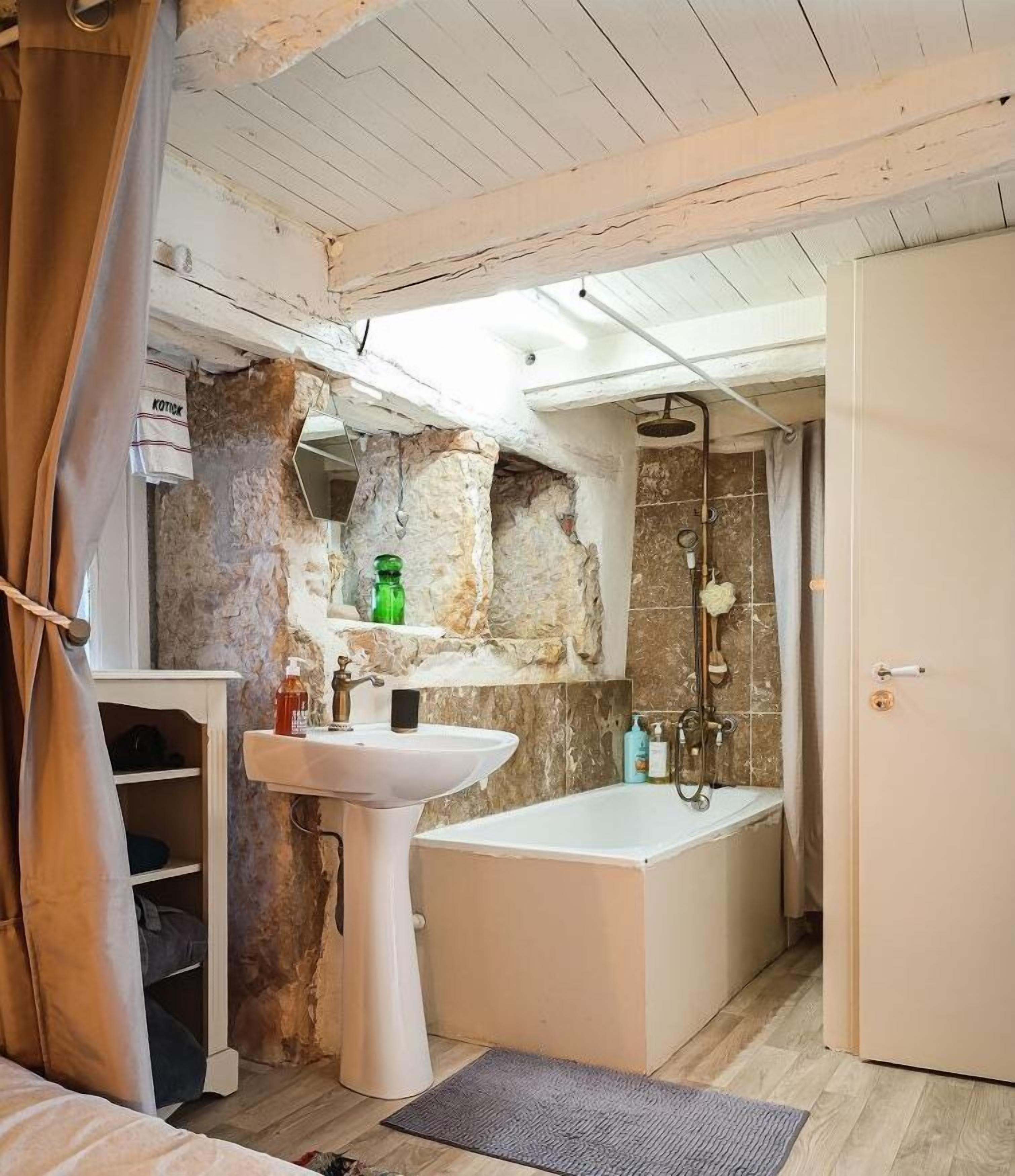 Une salle de bain rustique avec un mur en pierre, un lavabo blanc et une baignoire.