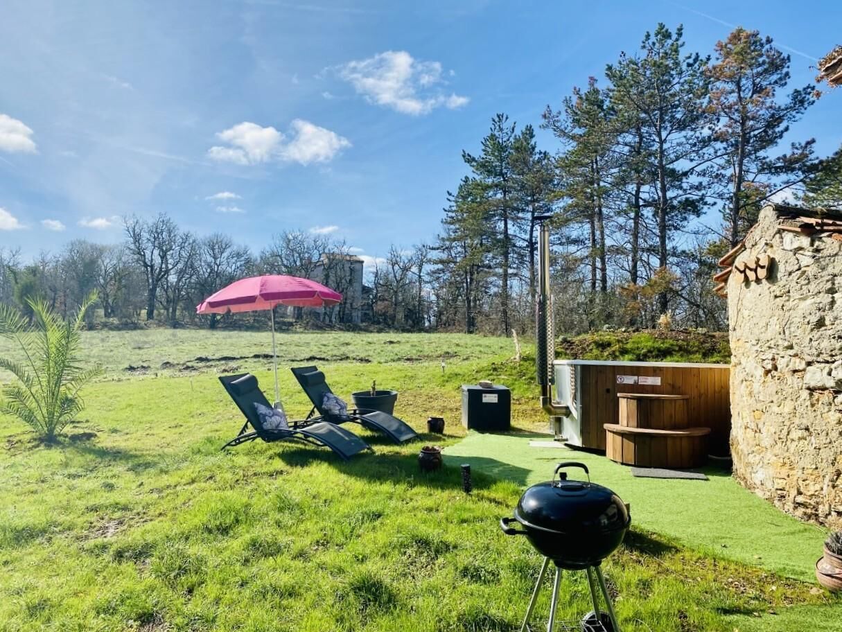 Un espace extérieur verdoyant, aménagé avec des chaises longues, un barbecue et une petite structure en bois.