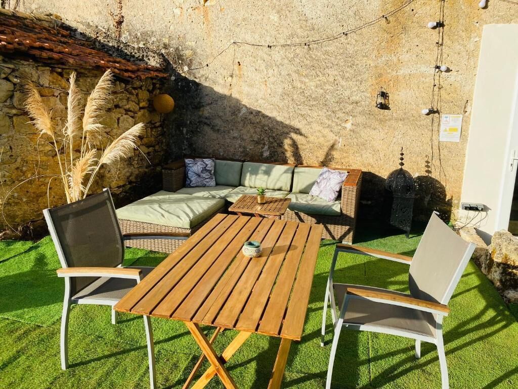 An outdoor seating area with a wooden table and chairs, a cushioned sofa, and a stone wall backdrop.