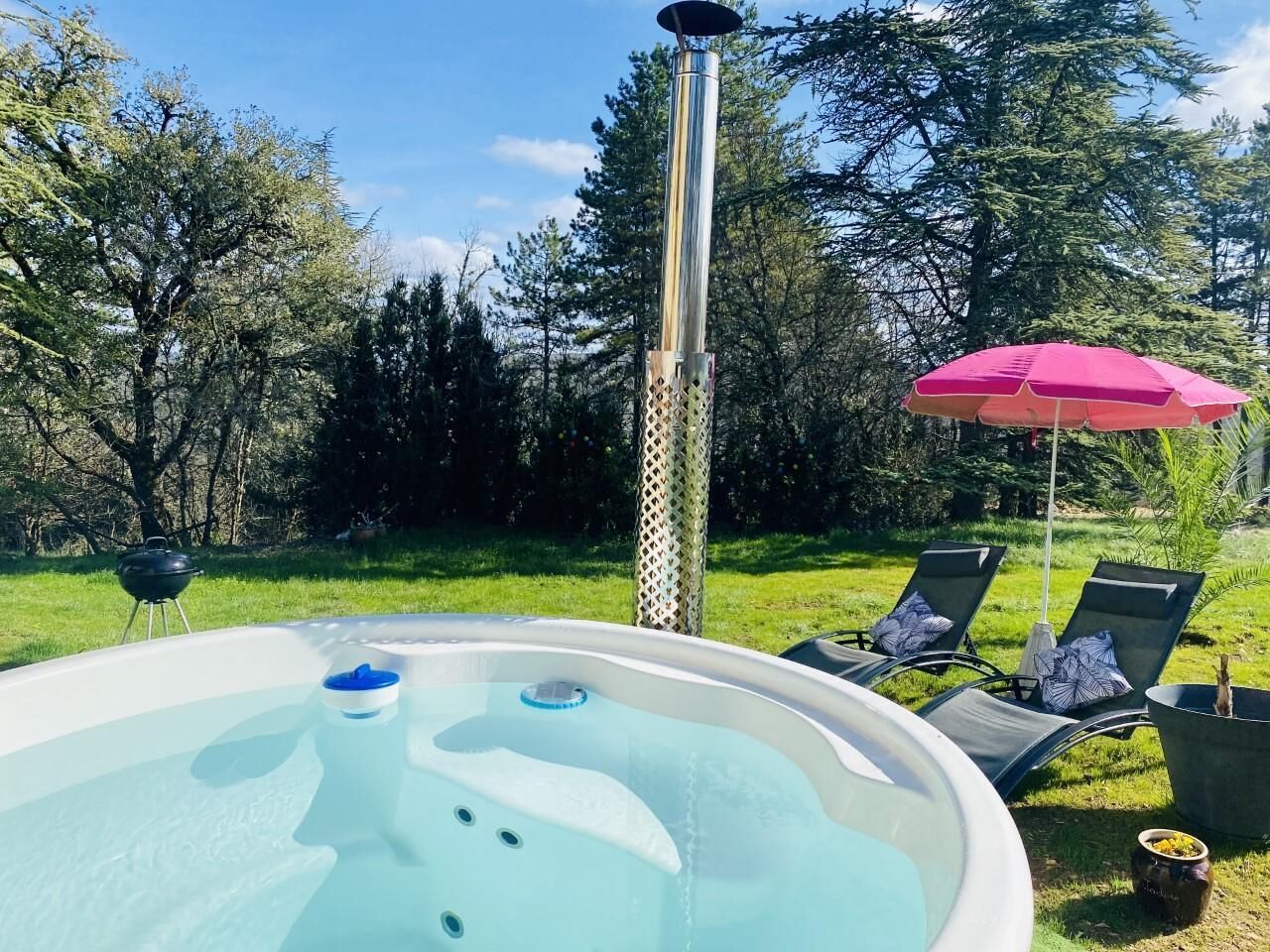 Un jacuzzi dans un jardin, avec un barbecue et des chaises longues.
