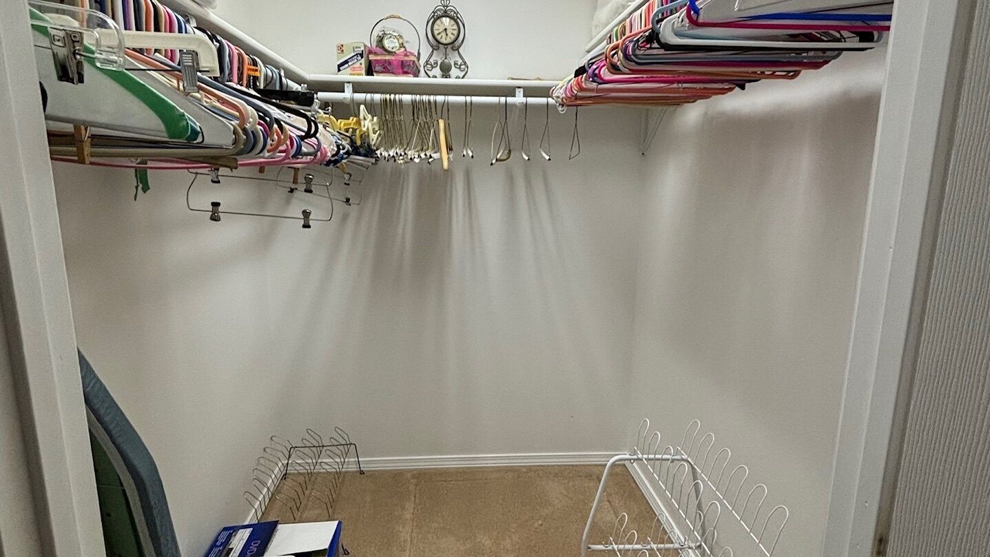 A closet with hanging clothes, a clock, and a shelf with various items.