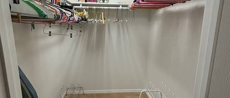 A closet with hanging clothes, a clock, and a shelf with various items.