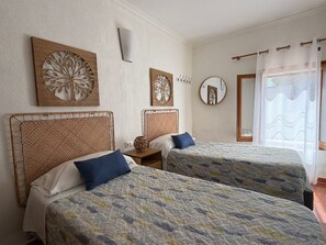 Une chambre avec deux lits, un miroir fixé au mur et une fenêtre avec un rideau.