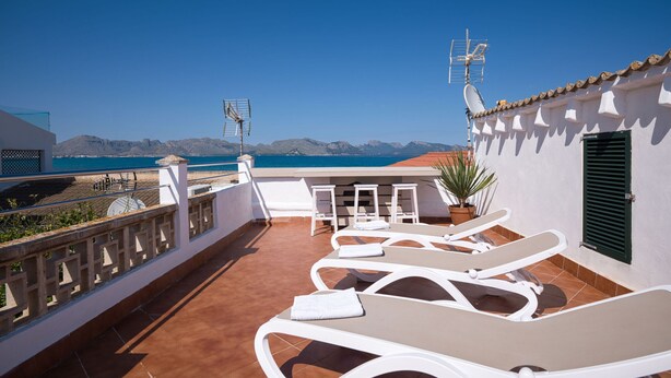A terrace with white lounge chairs, a small table, and a potted plant. - Nice house with 3 bedrooms, barbecue and private pool (Alcúdia)