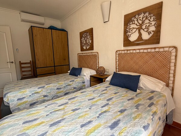 Une chambre avec deux lits, une armoire en bois, des œuvres d’art murales et une petite table.