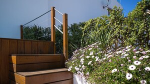 A wooden staircase leading to a white wall with a garden of white and purple flowers. - Nice house with 3 bedrooms, barbecue and private pool (Alcúdia)