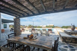 Un área de estar al aire libre con mesas y sillas de piedra, una piscina y vistas a edificios en la distancia.
