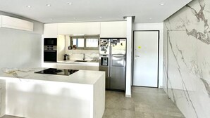 Une cuisine moderne avec des meubles blancs, un îlot central, des appareils en acier inoxydable et un dosseret en marbre.