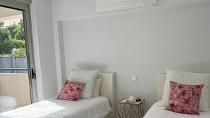 Une chambre moderne avec deux lits, chacun recouvert d’une couverture bleue et agrémenté de coussins à motifs floraux. On y trouve une petite table sur laquelle sont posés un livre et un objet décoratif.