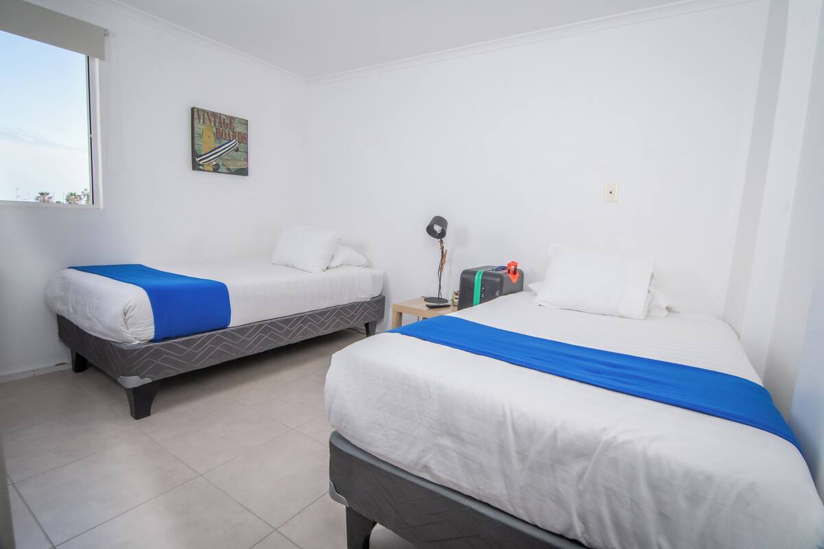 Camera d'albergo con due letti, una finestra, un'opera d'arte appesa al muro, un comodino con una lampada e una presa elettrica.
