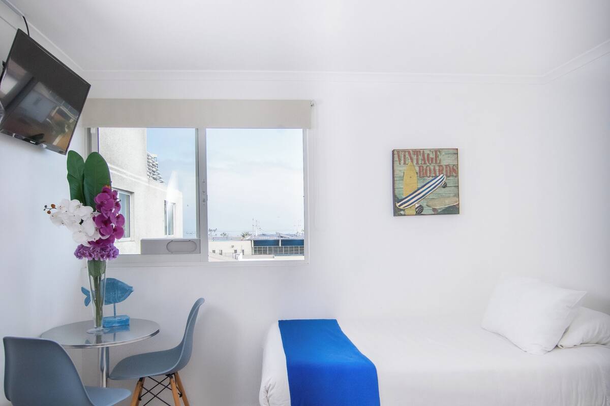 Una stanza con un letto, una scrivania, una sedia, una finestra e una lampada fissata al muro.