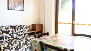 Ein Zimmer mit einer gepolsterten Couch mit Punkten, einem Esstisch mit einer blumigen Tischdecke, einer Holzkommode und einem großen Fenster mit Blick.