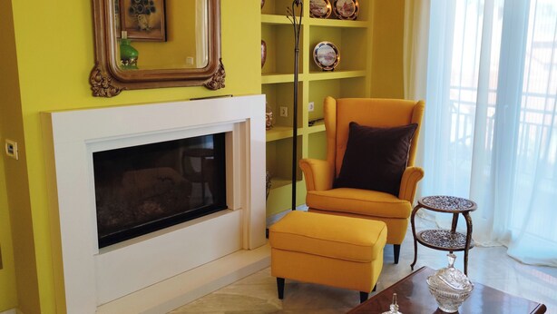 Un salon avec une cheminée, un fauteuil jaune, une table basse et un miroir décoratif.