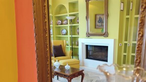 Une pièce dotée d’un grand miroir qui reflète un salon, une cheminée et un fauteuil jaune.