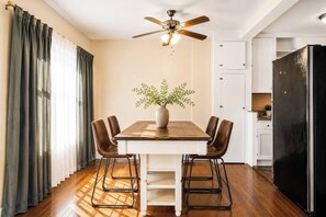 A dining area with a wooden table, four chairs, a vase with greenery, a ceiling fan, and a kitchen area with a black refrigerator. - King Bed 1BD 8 min to Downtown & Pier Pet-friendly (St. Petersburg)