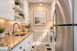 A kitchen with white cabinets, a granite countertop, stainless steel appliances, and a beach-themed painting on the wall. - King Bed 1BD 8 min to Downtown & Pier Pet-friendly (St. Petersburg)