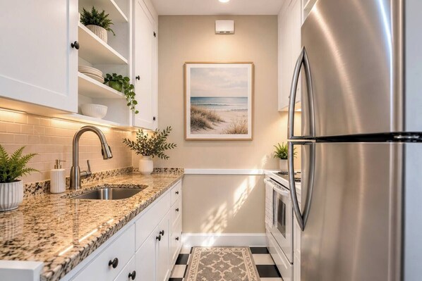 A kitchen with white cabinets, a granite countertop, stainless steel appliances, and a beach-themed painting on the wall. - King Bed 1BD 8 min to Downtown & Pier Pet-friendly (St. Petersburg)