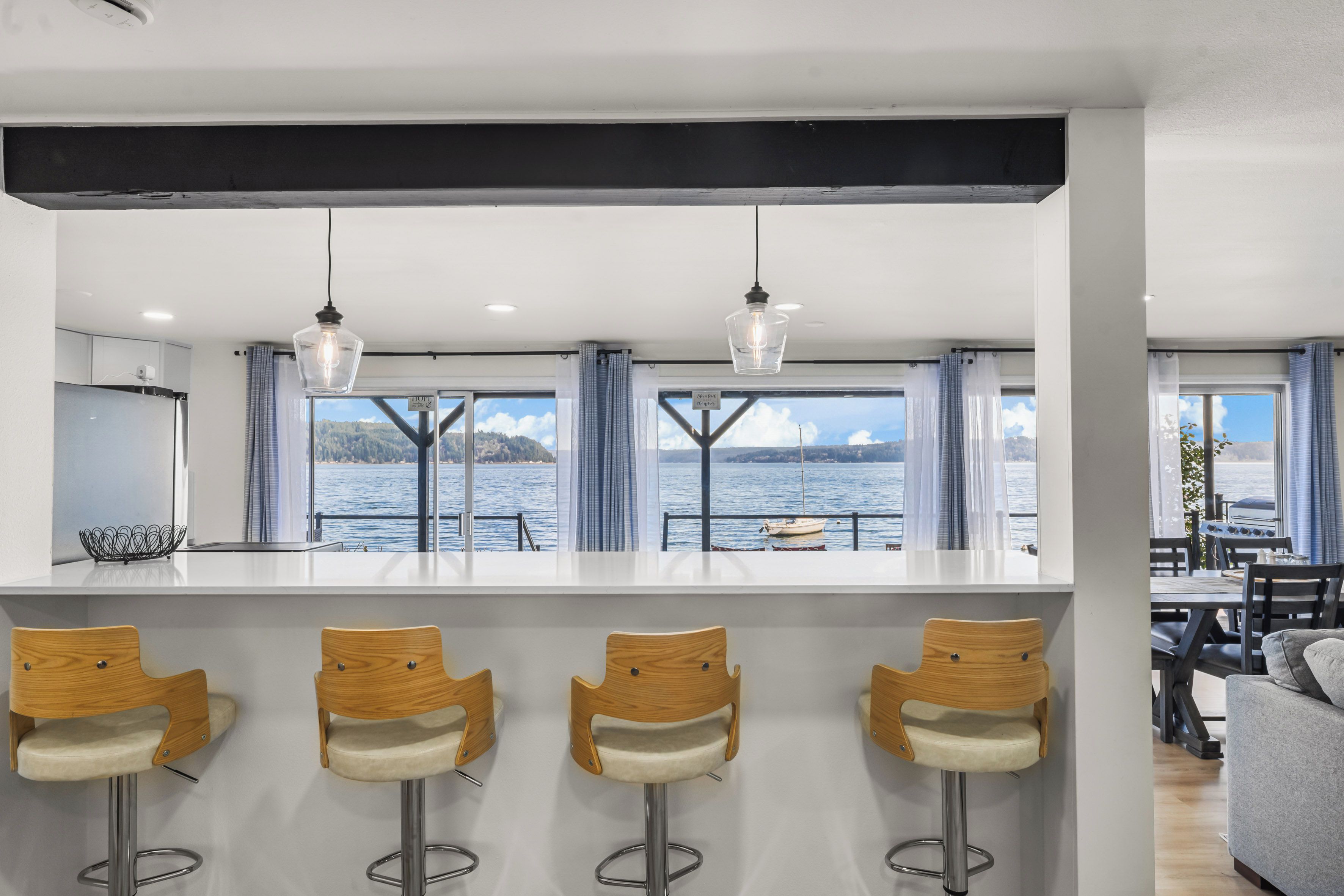 Een moderne keuken met een bar, grote ramen met gordijnen en uitzicht op het water.