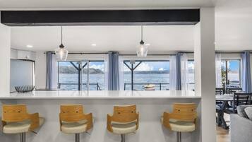 Een moderne keuken met een bar, grote ramen met gordijnen en uitzicht op het water.