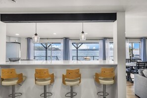 A modern kitchen with a bar area, large windows with curtains, and a view of the water. - Hood Canal Pearl - Waterfront, Hot tub, canal views (Shelton)