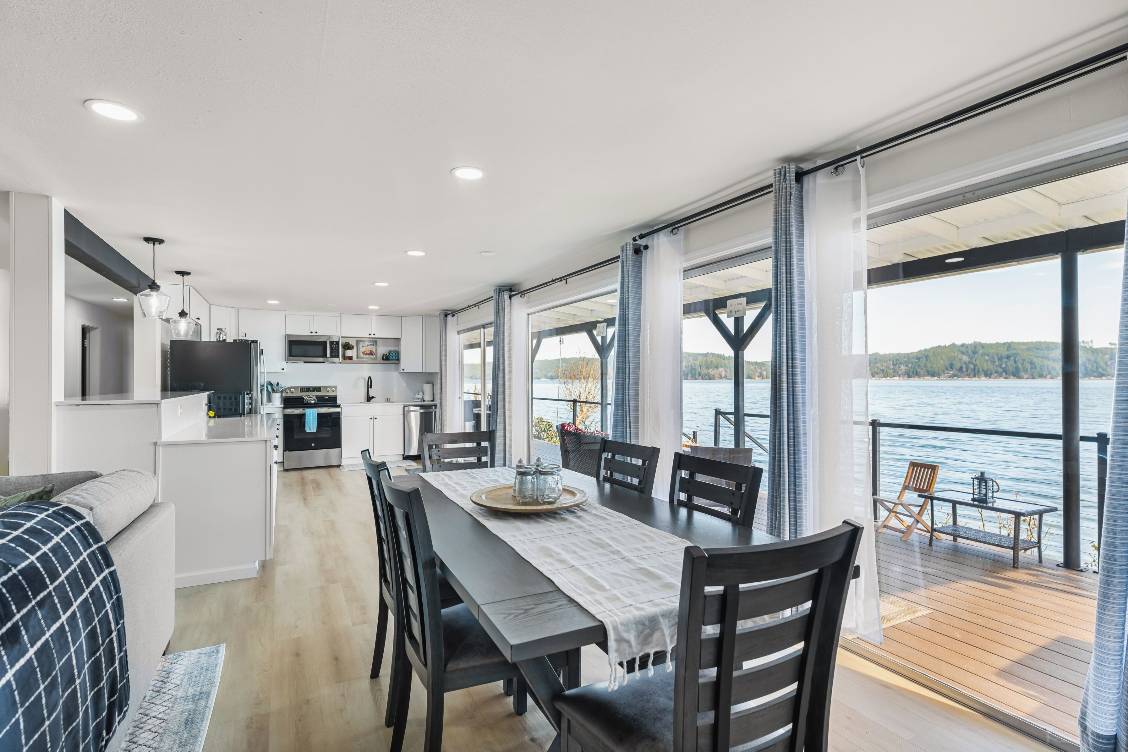 A modern kitchen with white cabinets, a dining area with a table and chairs, and a view of a lake through large windows.