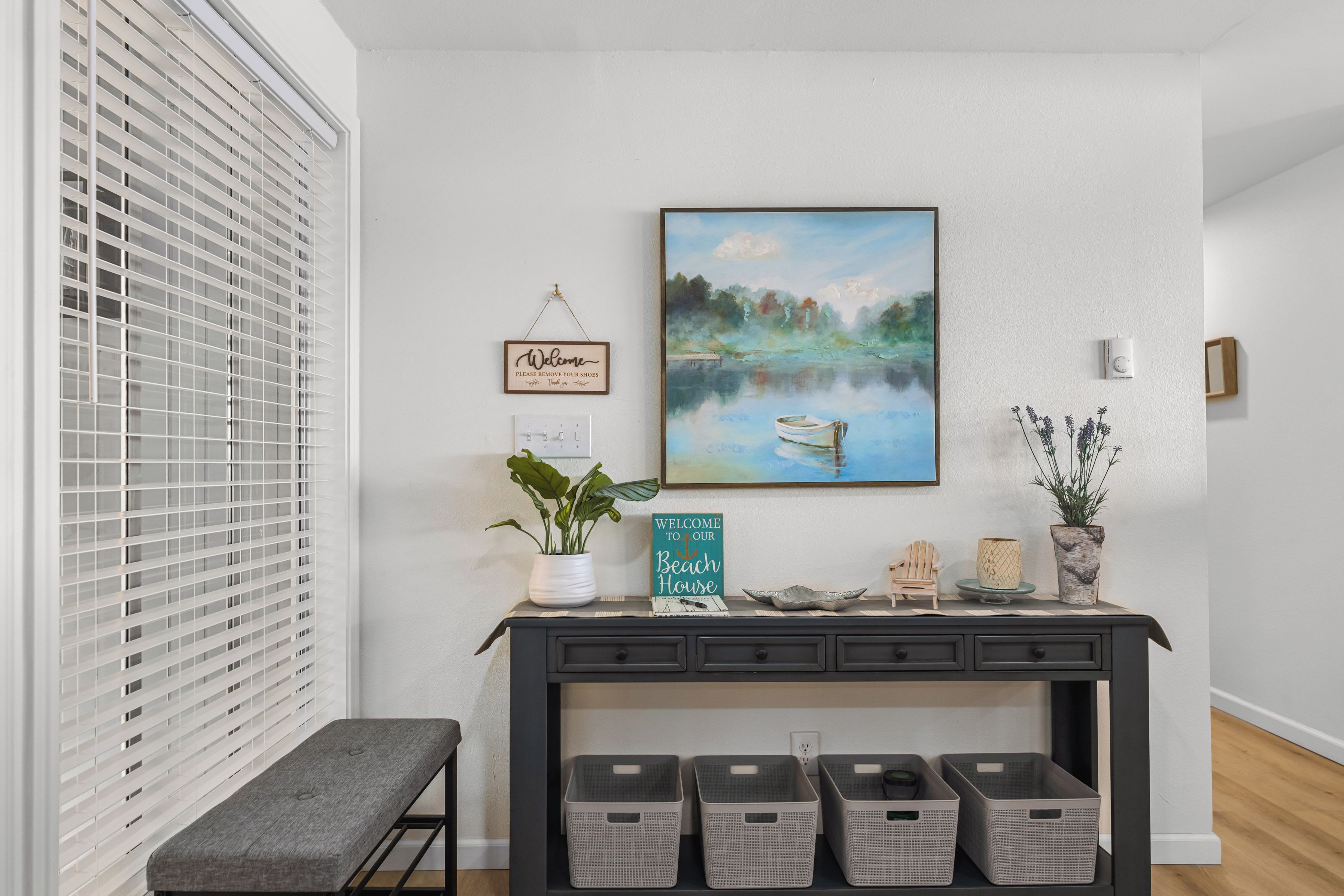 A modern entryway with a bench, a welcome sign, a painting of a lake, and a sign indicating a beach house.