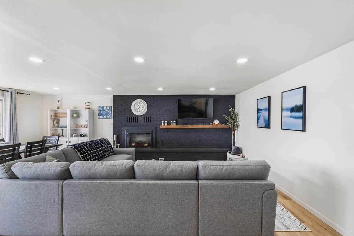 Ein modernes Wohnzimmer mit einem grauen Sofa, einem Kamin und einem Fernseher.