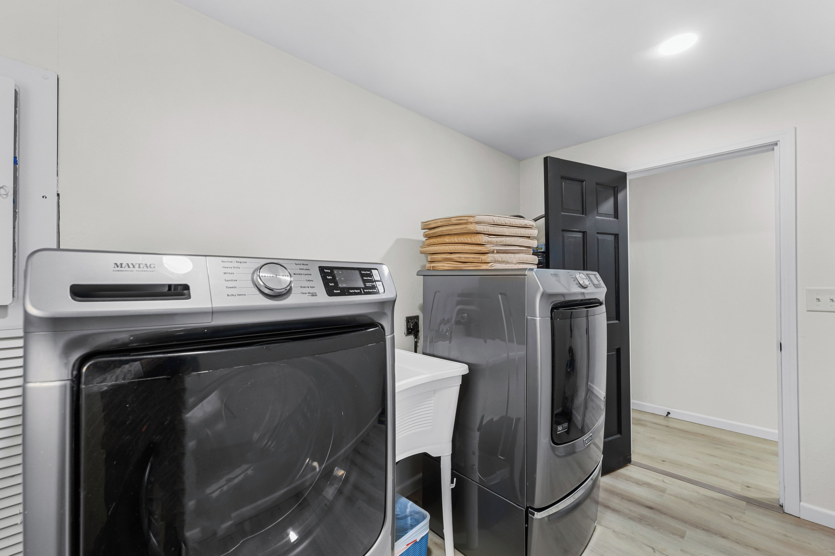 A laundry room with two Maytag washers and dryers, a white laundry basket, and a door to another room.