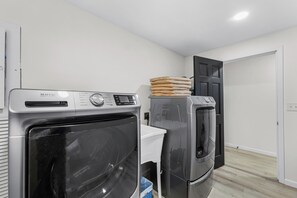 A laundry room with two Maytag washers and dryers, a white laundry basket, and a door to another room. - Hood Canal Pearl - Waterfront, Hot tub, canal views (Shelton)