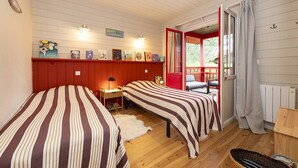 Une pièce confortable avec deux lits, un coin lecture avec des livres et une fenêtre donnant sur un espace verdoyant.