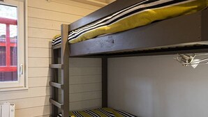 Un lit superposé avec une literie à rayures, une fenêtre avec un cadre rouge et un radiateur.