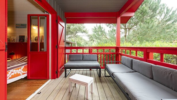 Une véranda aux couleurs rouge et blanche, avec un canapé, deux fauteuils et une petite table.