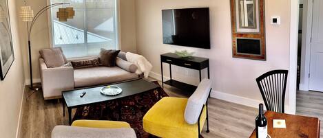 A living room with a sofa, a coffee table, a TV, and a dining area with chairs and a table.