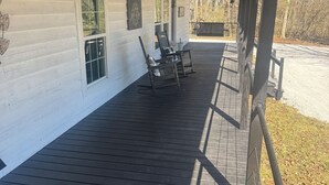 Un espace extérieur abrité doté d’une terrasse en bois, de deux fauteuils à bascule et d’un bâtiment blanc avec des fenêtres et une porte.