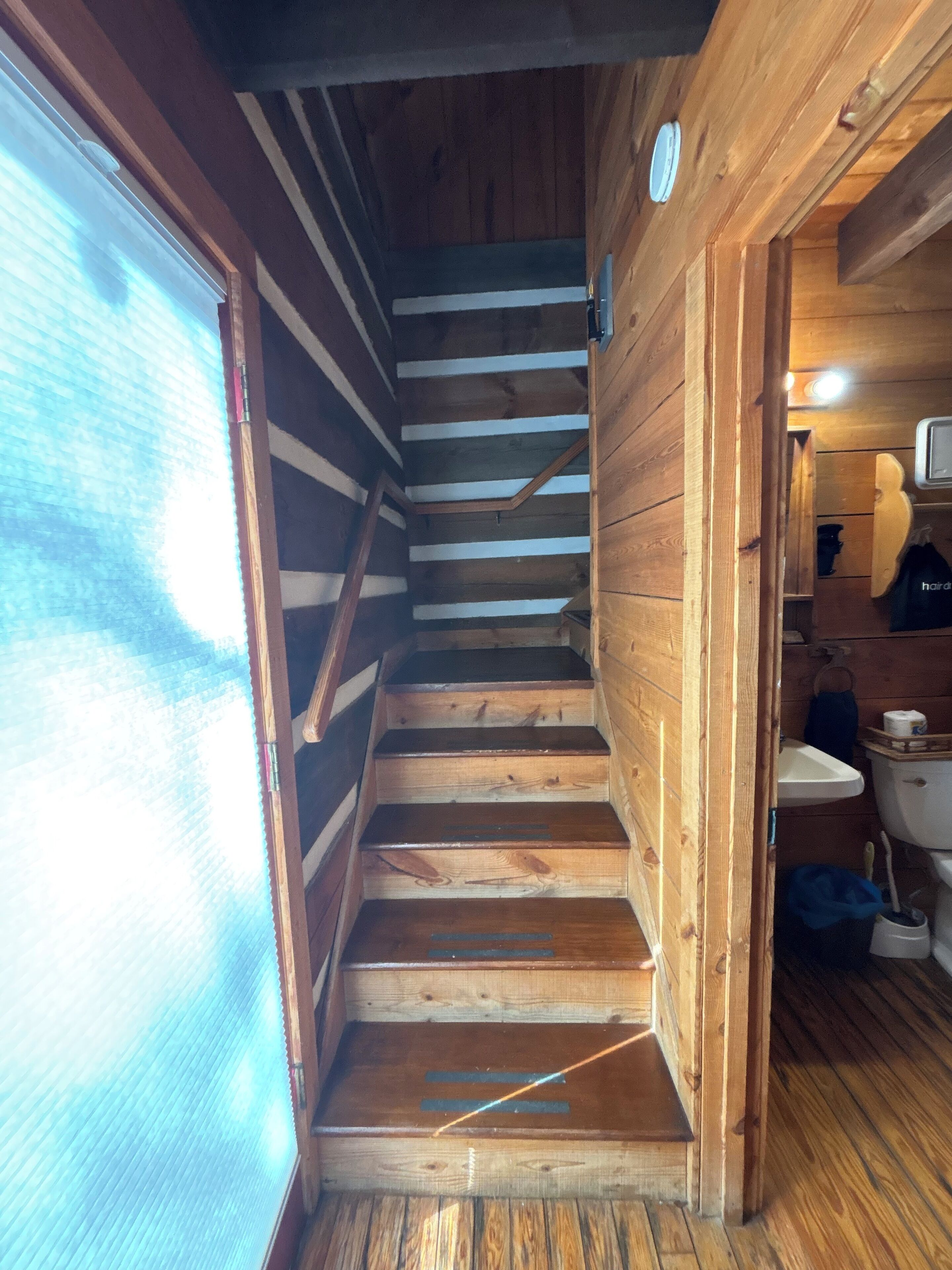 A wooden staircase leading to a bathroom with a sink and toilet.