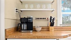 Une cuisine équipée d’une machine à café, d’un récipient rempli de capsules de café et d’un bloc à couteaux posé sur le plan de travail.