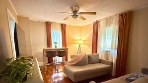 Un salon avec un canapé, un bureau avec une chaise, un ventilateur de plafond et une lampe.
