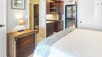 A bedroom with a bed, dresser, and a view of the kitchen and balcony.