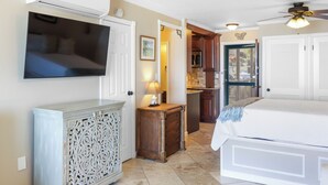 Une chambre à coucher avec un lit, un téléviseur fixé au mur, une armoire en bois et, au fond, un coin cuisine.