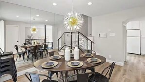 Ein moderner Essbereich mit einem runden Tisch, gedeckt für sechs Personen, einer besonderen Pendelleuchte und einer Treppe, die zu einer anderen Ebene führt.