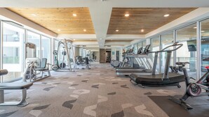 Een sportschool met cardioapparatuur, krachtapparaten en een kamerbreed tapijt met dessin.