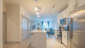 Een moderne keuken met een centraal eiland, roestvrijstalen apparatuur en een eethoek met blauwe gordijnen.