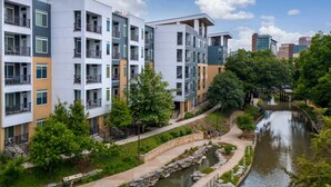 Een modern appartementencomplex met meerdere balkons, een rivier langs de zijkant en een verzorgde tuin.