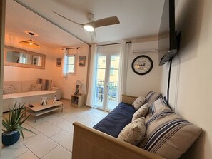 Une pièce comprenant un lit, un canapé, un ventilateur de plafond, un téléviseur fixé au mur et une fenêtre avec des rideaux.