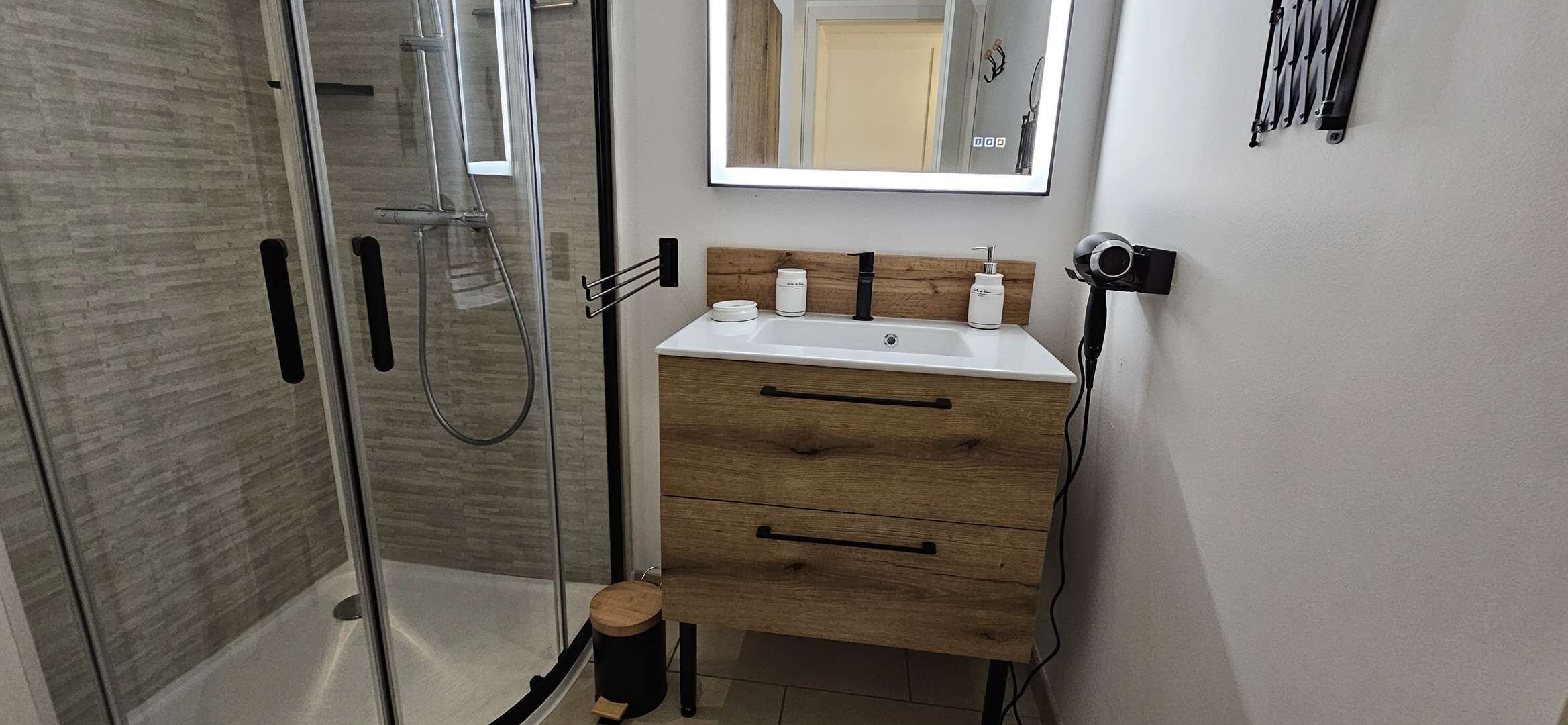 Ein Badezimmer mit Duschkabine aus Glas, einem Holzbidet und einem Spiegel über dem Bidet.