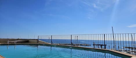 A swimming pool with a view of the ocean, a metal fence, and a wooden deck.