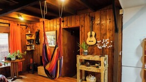 Una stanza accogliente con pareti in legno, un'amaca, una chitarra e un piccolo tavolino in legno con una pianta e un vaso.