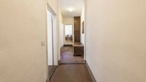 A narrow hallway with a tiled floor, an arched doorway, and a view into a room with a wooden bench and chairs. - Classic Florence A By MMega (Firenze)