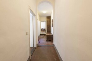 Un pasillo estrecho con suelo de baldosas, un arco de entrada y vistas a una habitación con un banco y sillas de madera.