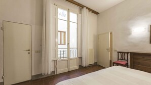 A bedroom with a bed, a door, a window with curtains, a radiator, and a wooden dresser. - Classic Florence A By MMega (Firenze)